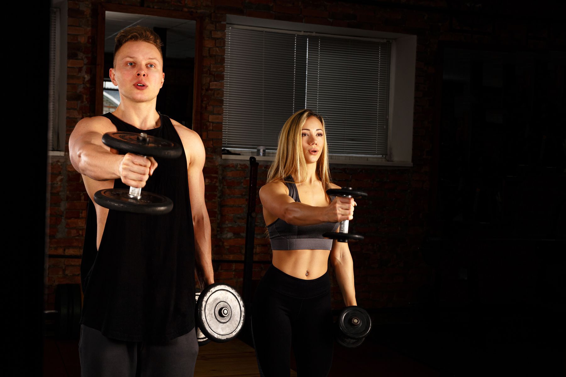 Man and woman strength training with dumbbells in a gym